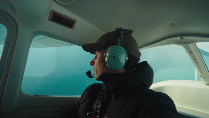 Man with headset cap and black coat travels by airplane
