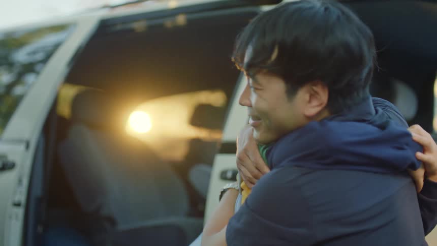 Father and son hug lovingly next to a car at morning