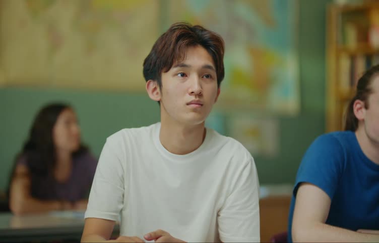 A student sits at the desk next to their classmate and then raises their hand to answer a question