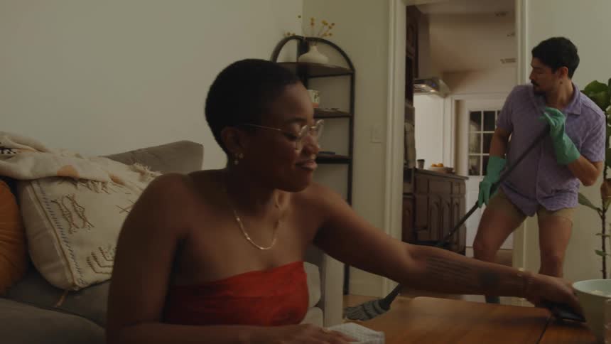 Woman cleans coffee table man dances while mopping