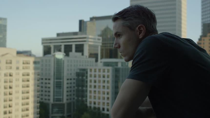 A man leans over the railing viewing a city
