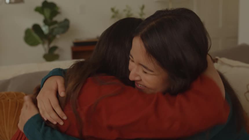Friends are smiling and hugging each other while sitting on a couch