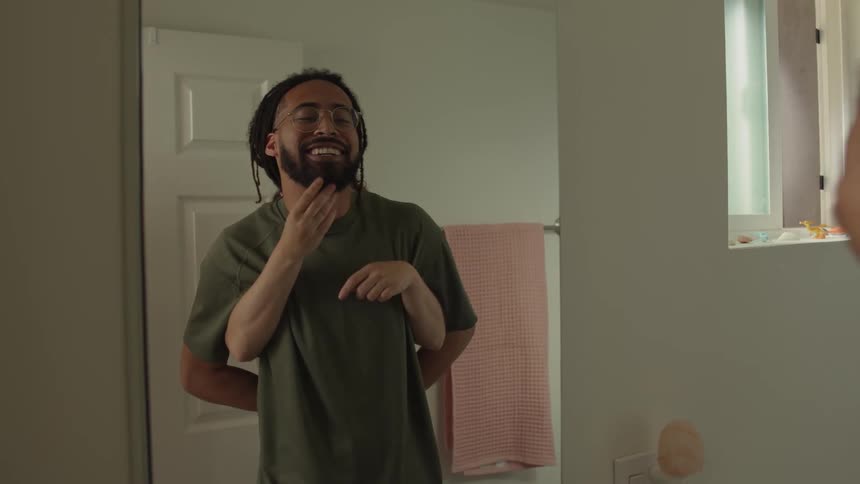 A man playing in front of the mirror with his hands behind his back and another person behind him hiding and gesturing with their arms while playing in front of the mirror