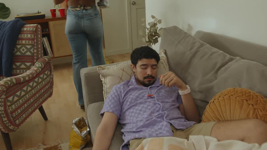 Man lies on couch while woman cleans around him