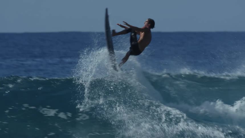 A surfer rides a big wave and leaps in the air and spins before landing back in the water