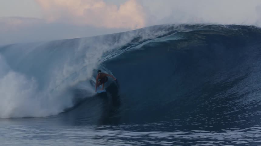 Man rides a wave with a surfboard at evening