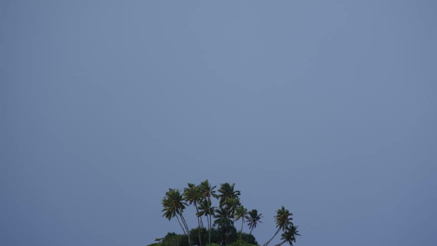 A reveal of a small tropical island in the ocean under clear blue skies