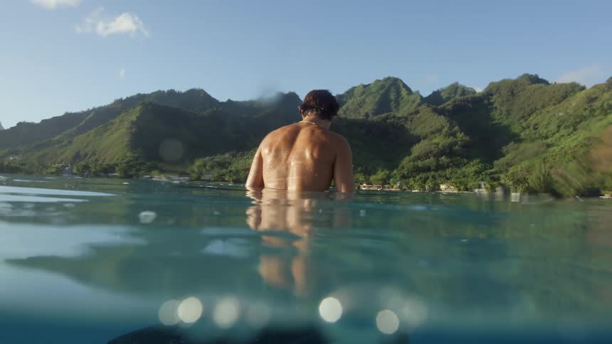 A man is sitting on his surfboard in the ocean