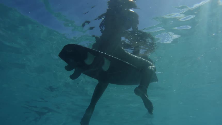 A surfer sits on her surfboard in a calm sea