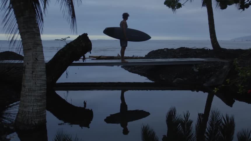 A surfer is standing on the beach watching the sunset