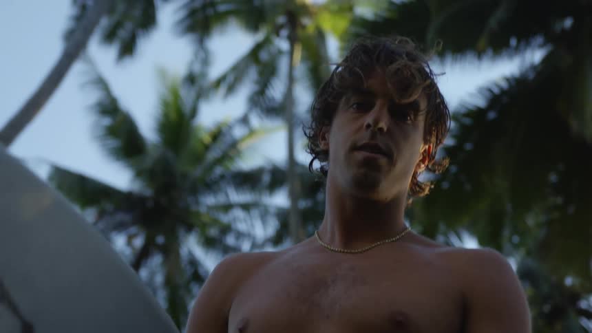 A man on an island with palm trees holding a surfboard