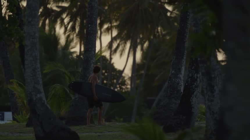 A man holding a surf board walking towards the beach on a tropical island