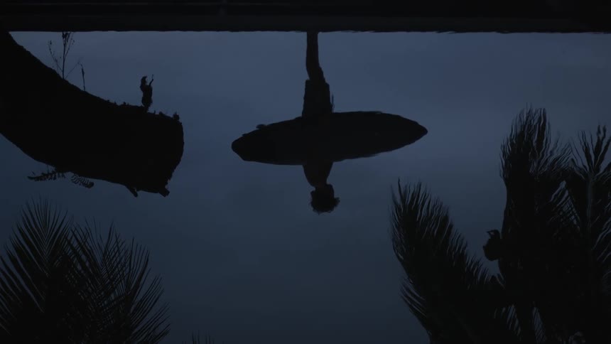 Reflection in a lake of a young man holding a surfboard