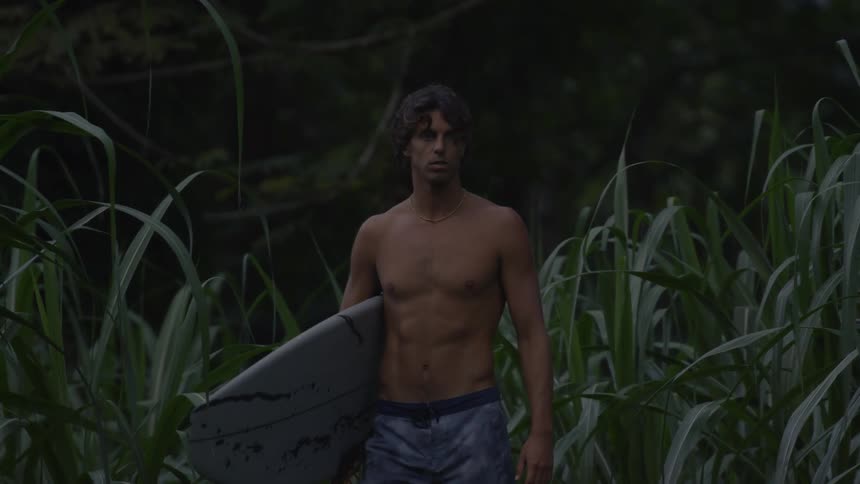 Man in a tshirt holding his surfboard walking in a natural environment