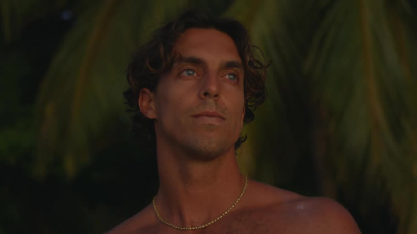 Portrait of a young shirtless man standing outdoors with a contemplative face expression next to plants and leaves