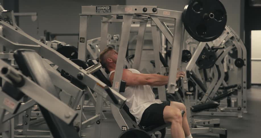 A man is sitting in a weight lifting machine in the gym working his arms with heavy weights