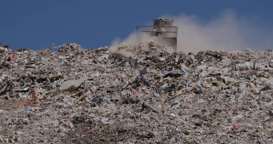 Bulldozer pushing trash in dump creates dust