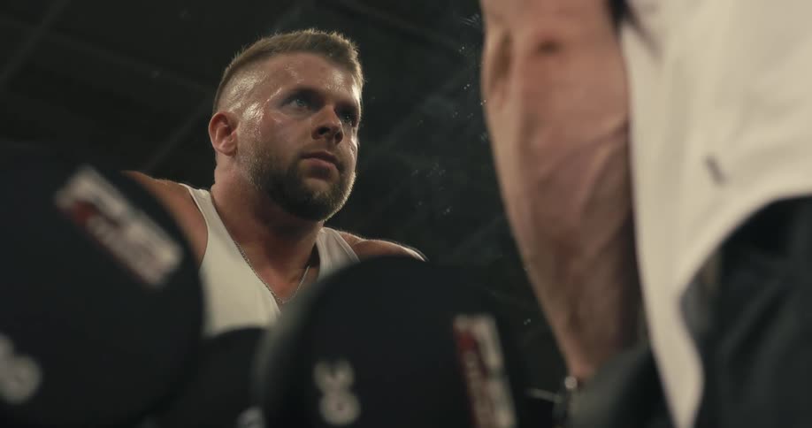 A man is in a gym looking at himself in the mirror as he picks up a barbell with weights and walks away