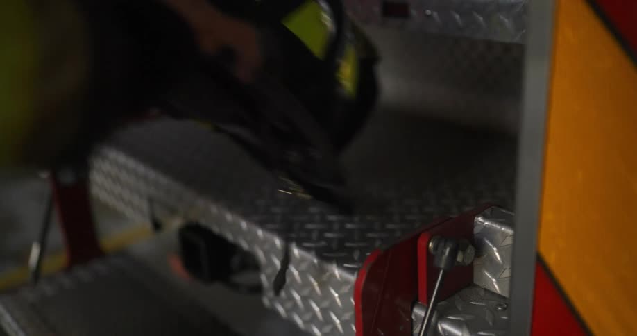 Person wearing firemans jacket picks up hat off back of truck