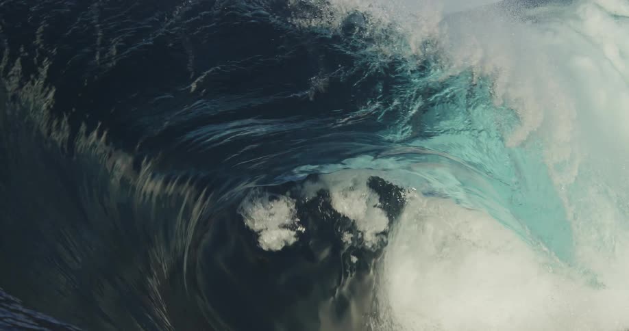 The sun shines on a clear blue wave as it curls and splashes as it rolls in