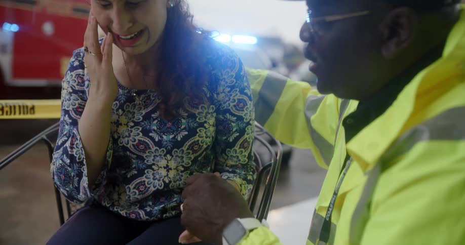 Public official talking and shaking hands with a seated crying woman with fire vehicles in the background