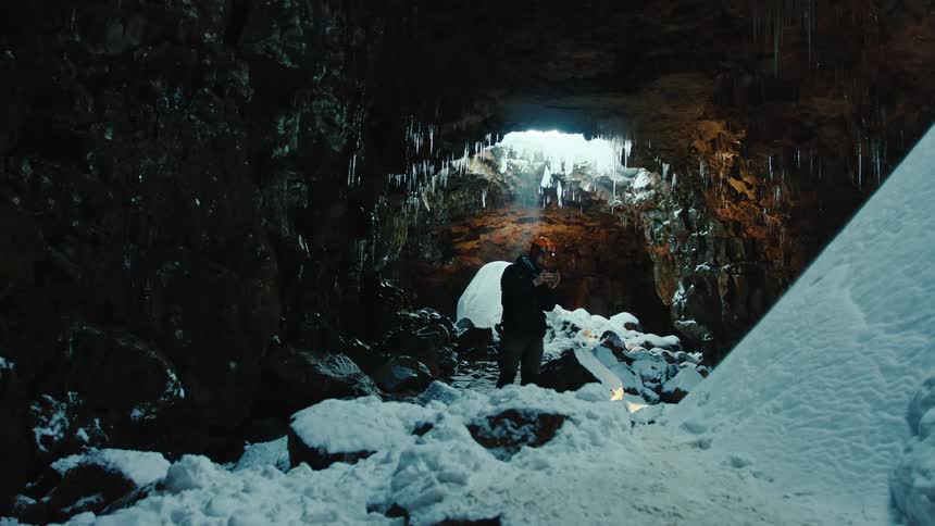 A person wearing a helmet standing in a cave covered in snow and ice while using a light to examine something