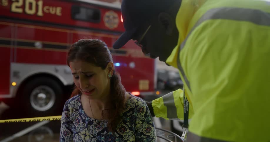 A woman sits crying being comforted by a man and a fire truck behind her