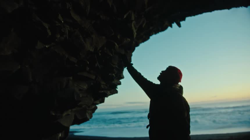 A man touching rocks near a beach at sunset