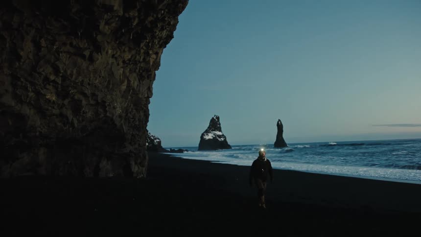 Man walking alongside a beach and a cave
