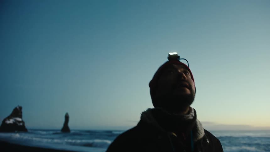 Man with a headlamp walking toward a cave on a beach