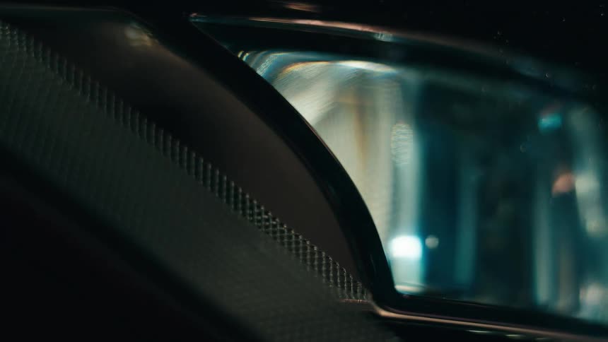 Passing lights reflect on the headlighst of a car