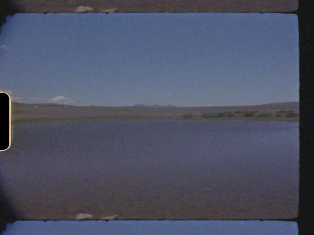A small lake surrounded by land and bushes in the middle of the day