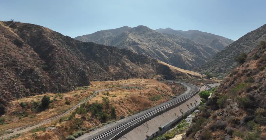 Road and train tracks cut through valley between scrub covered mountains