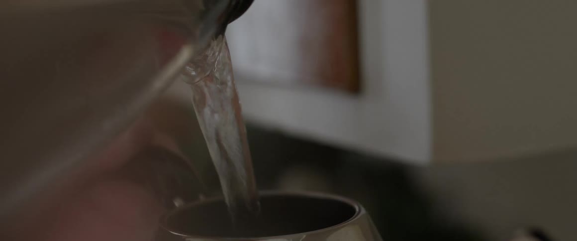 Water being poured out of a pitcher into a mug by a person in their kitchen