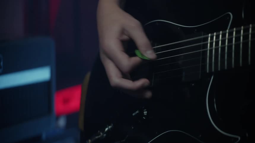 A hand using a pick to play electric guitar