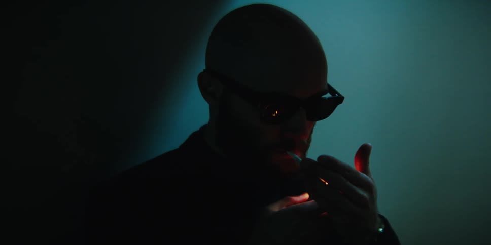 A man wearing glasses lights a cigarette