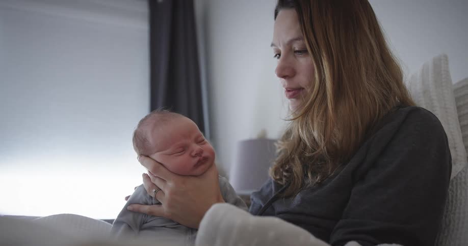 Mother sitting in bed supports babys head while stroking childs back