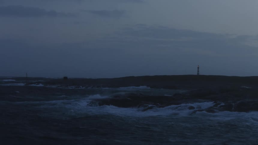Ocean waves crashing on a small rocky island with a lighthouse