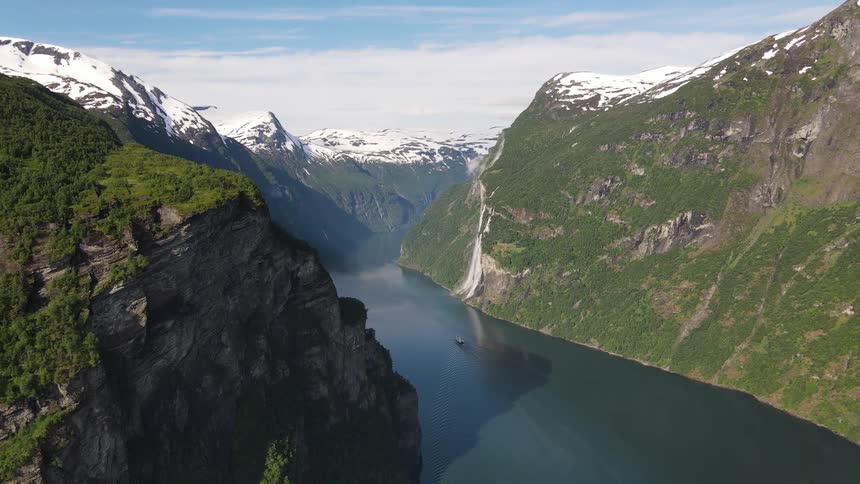 A boat sails on a river between mountains with mountains in the distance