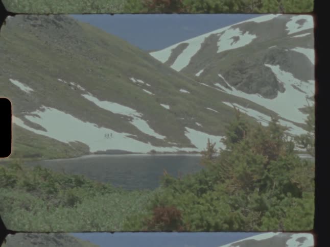 A lake at the bottom of a mountain covered in snow and surrounded by plants