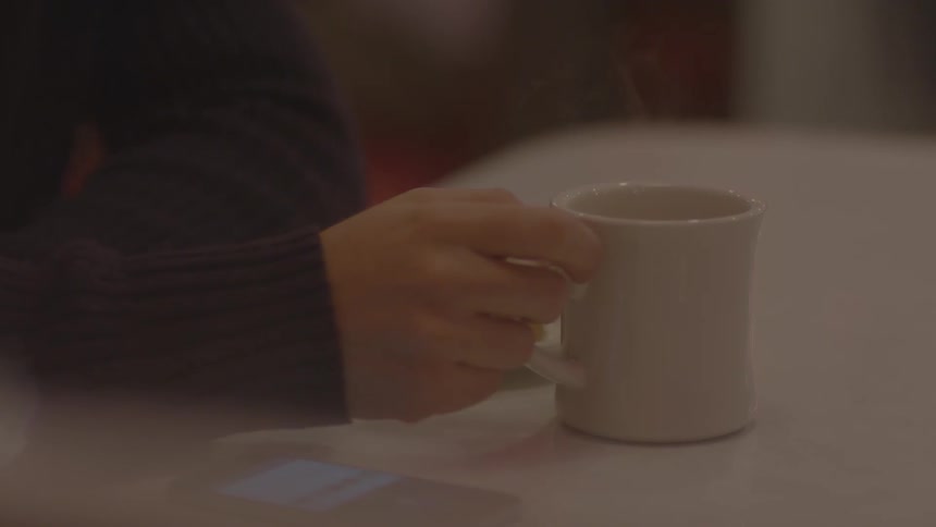 Steam rising from a warm cup that is being held by someone at a table