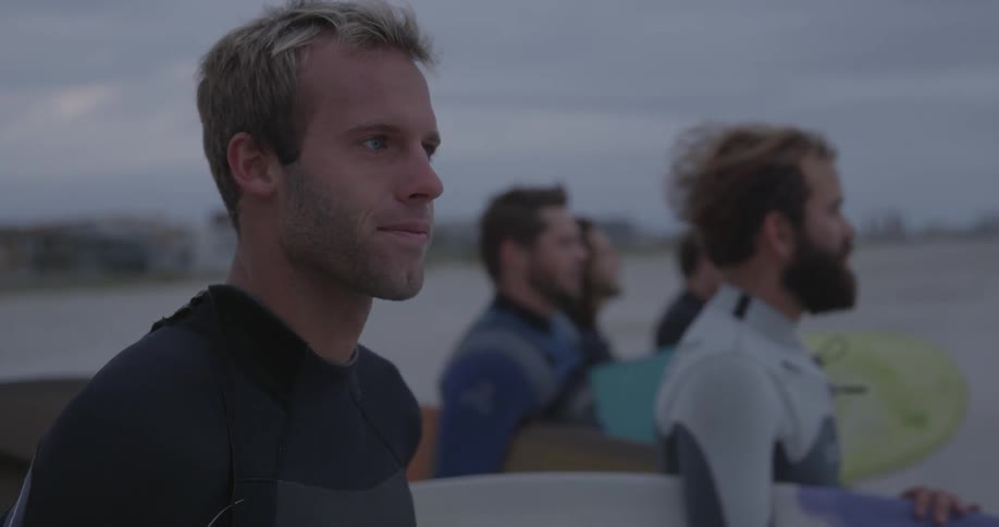 Men in wetsuits carry surfboards on the beach