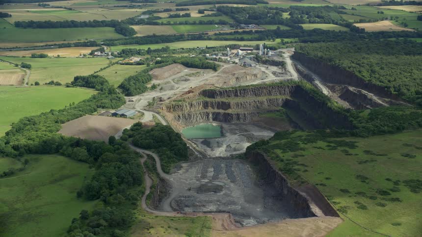 A small quarry with a lake inside in the middle of fields of grass