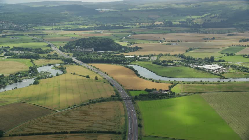 Drone view of a roadway through a flat land in a rural area on a bright sunny day