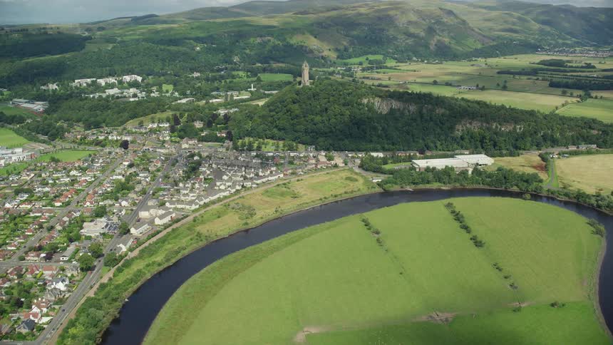 A huge field of grass with a river surrounding it and on the other side is a rural town