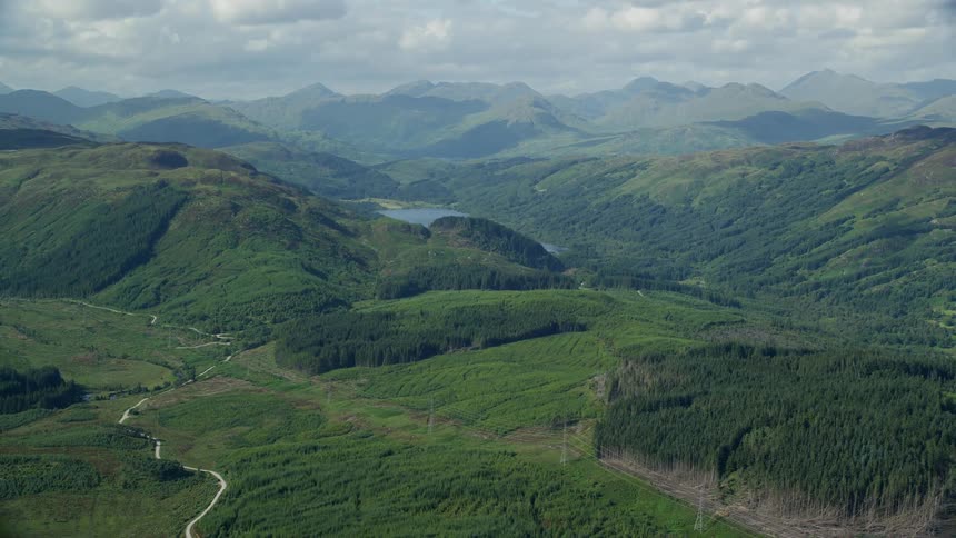 Drone view of a mountain landscape covered in forest trees with a small lake in the valley