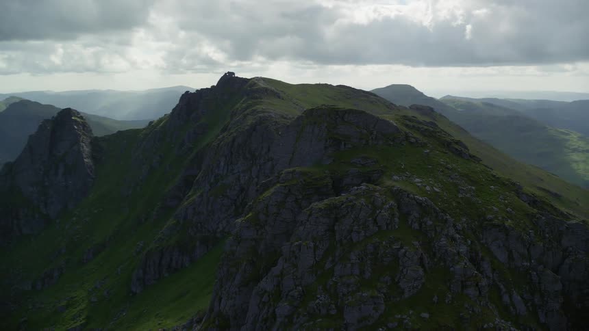A road runs up a steep mountainside with rocky cliffs and mountains in the distance