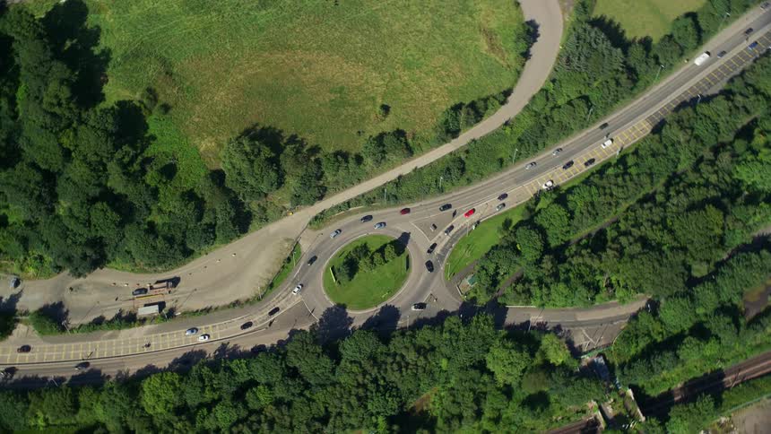 Aerial of a round about intersection with traffic going both ways among trees on a bright sunny day
