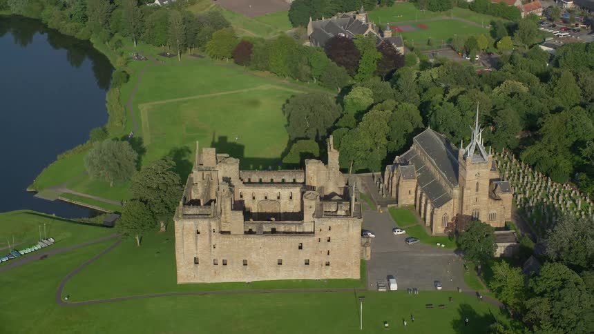 Aerial of a castle manor on a lush green lawn near a lake on a bright sunny day