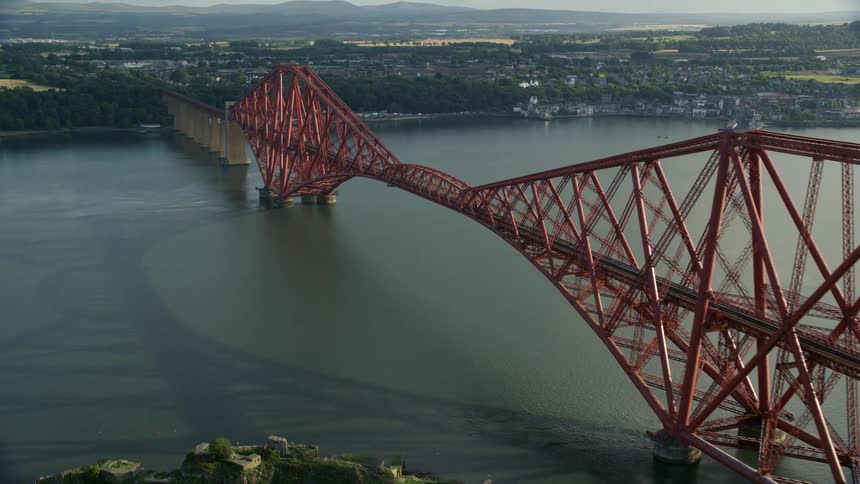 Drone view of an archway bridge over a large river leading to a suburban area with a flat landscape